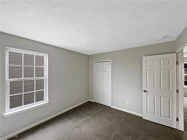 unfurnished bedroom with a closet, dark carpet, a textured ceiling, and baseboards