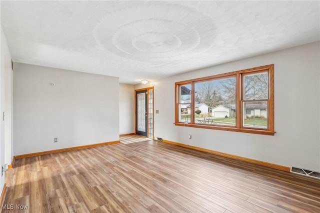 unfurnished room featuring light wood finished floors, visible vents, and baseboards