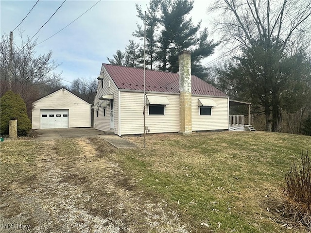 back of house with a lawn, driveway, a detached garage, an outdoor structure, and metal roof