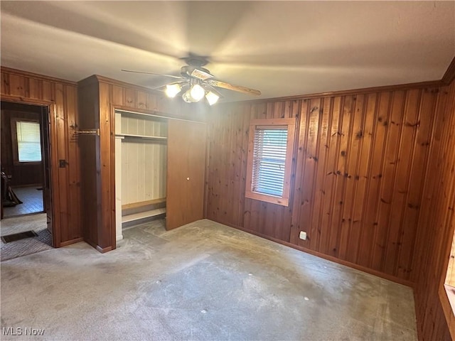 unfurnished bedroom with crown molding, wood walls, carpet floors, a closet, and a ceiling fan