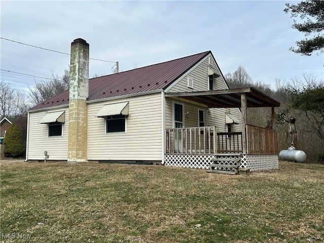 rear view of property featuring a standing seam roof, a lawn, a chimney, and metal roof