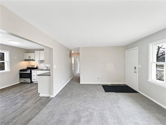 unfurnished living room featuring a sink, dark colored carpet, and baseboards