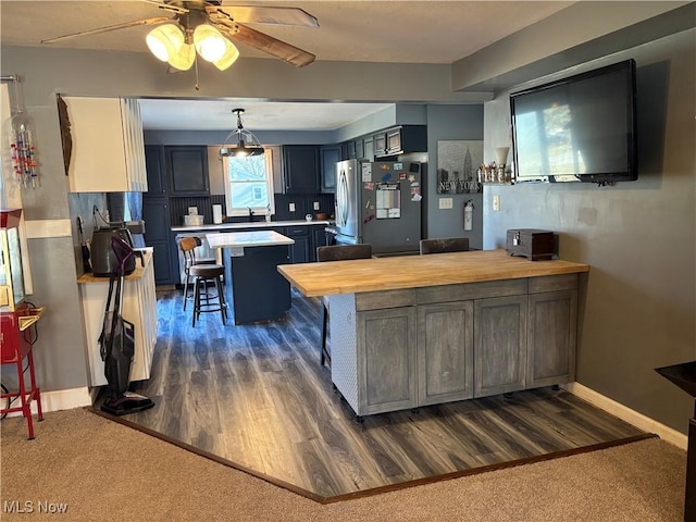 kitchen with dark wood-style floors, freestanding refrigerator, a peninsula, a breakfast bar area, and wooden counters