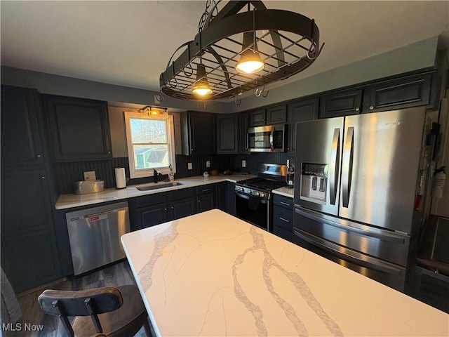 kitchen featuring light stone countertops, a sink, hanging light fixtures, appliances with stainless steel finishes, and dark cabinets