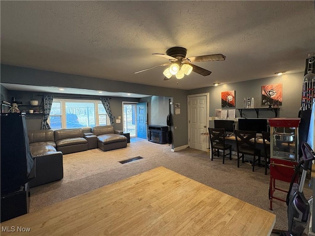 carpeted living area with visible vents, baseboards, a textured ceiling, and a ceiling fan