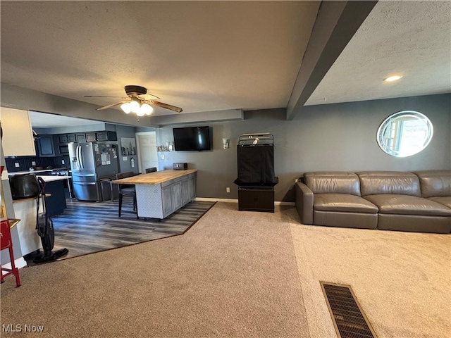 living area featuring visible vents, a textured ceiling, baseboards, and dark colored carpet