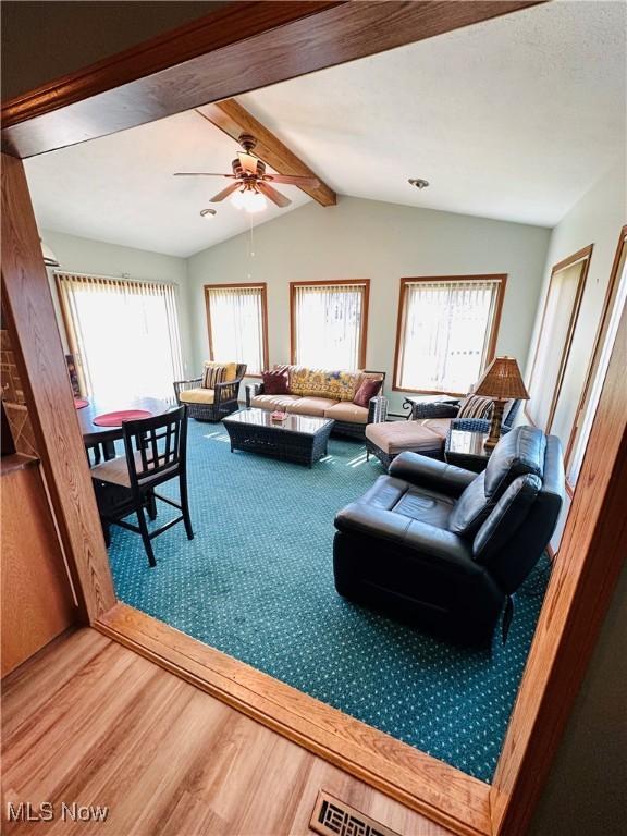 living room with a wealth of natural light, vaulted ceiling with beams, a ceiling fan, and wood finished floors