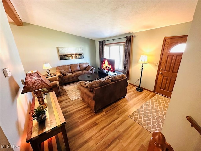 living area with baseboards, lofted ceiling, a textured ceiling, and light wood-style flooring