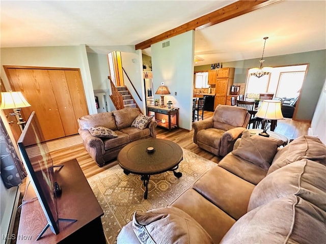 living room with visible vents, stairway, lofted ceiling with beams, wood finished floors, and a notable chandelier