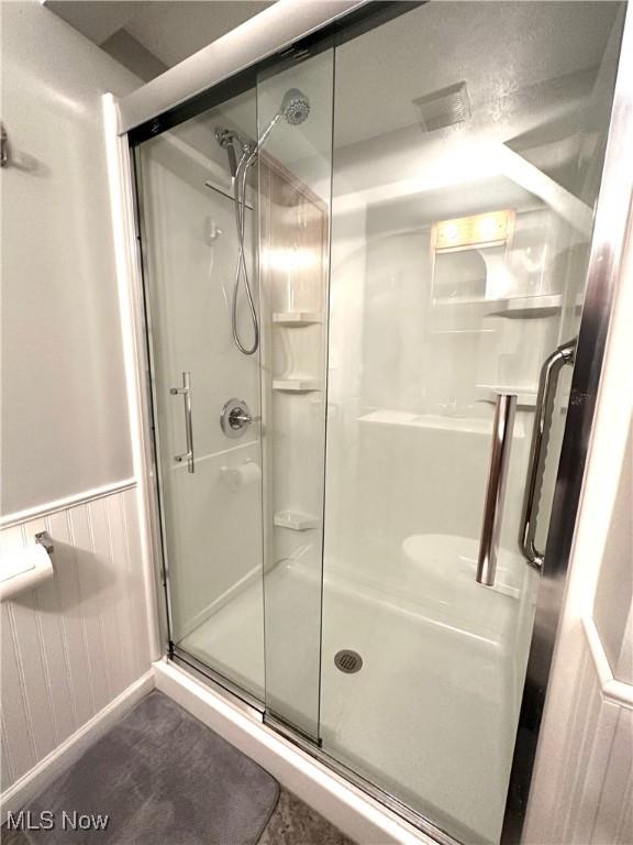 bathroom with a wainscoted wall and a shower stall