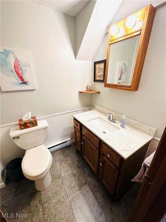 bathroom with a baseboard heating unit, toilet, a wainscoted wall, and vanity