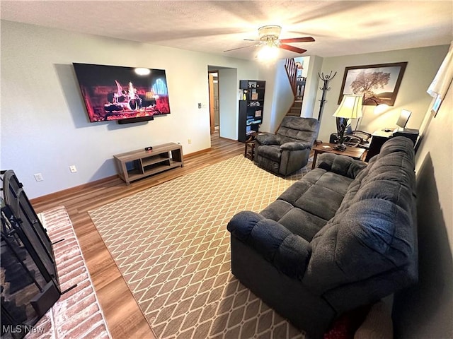 living area with ceiling fan, a textured ceiling, baseboards, and wood finished floors