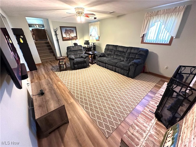 living area featuring stairway, wood finished floors, baseboards, visible vents, and ceiling fan