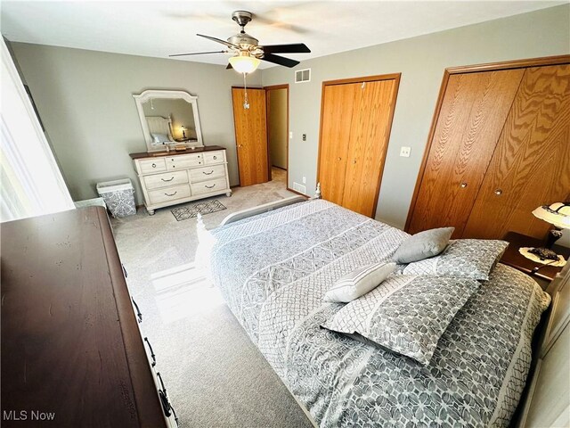 bedroom featuring visible vents, carpet flooring, a ceiling fan, and multiple closets