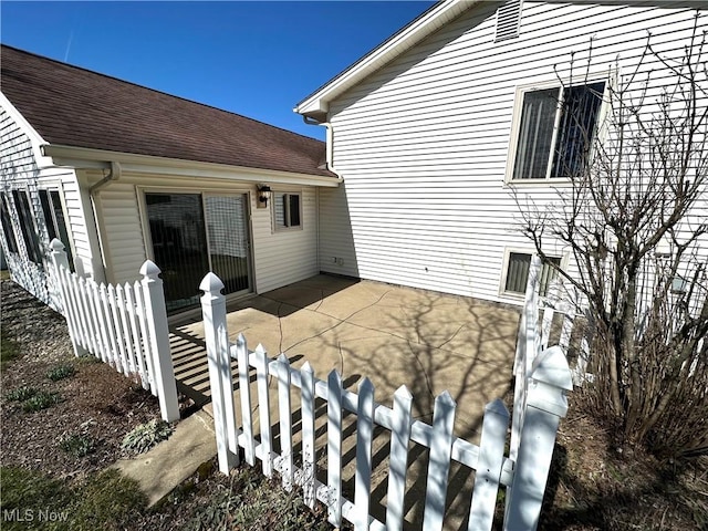 view of property exterior with a patio area, roof with shingles, and fence