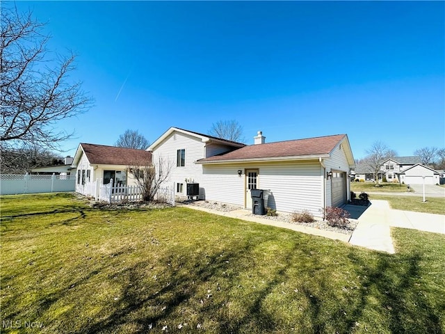 rear view of property with fence, central AC unit, an attached garage, a yard, and a chimney