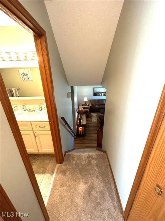 corridor with an upstairs landing, light carpet, a sink, a textured ceiling, and baseboards