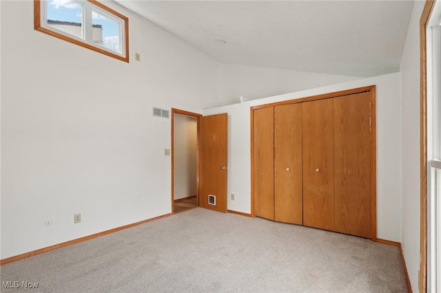 unfurnished bedroom featuring visible vents, a closet, carpet floors, baseboards, and vaulted ceiling