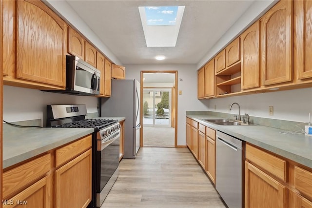 kitchen featuring a skylight, light wood-style flooring, a sink, light countertops, and appliances with stainless steel finishes