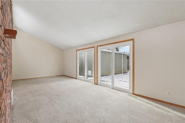 carpeted empty room with visible vents, a textured ceiling, a fireplace, baseboards, and vaulted ceiling