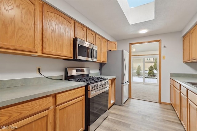 kitchen featuring light wood-style flooring, appliances with stainless steel finishes, a skylight, and light countertops