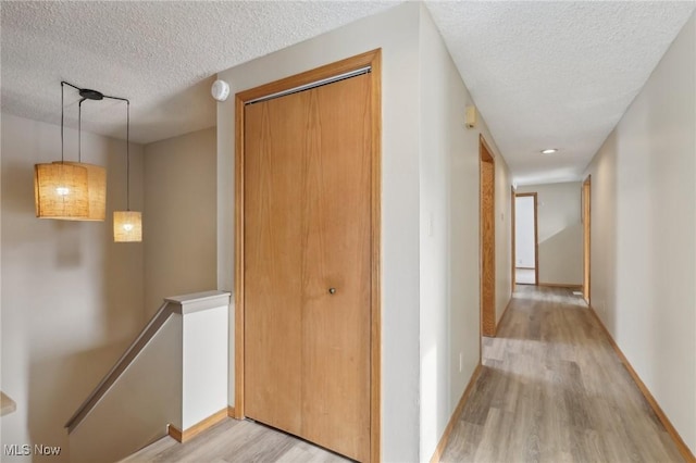 hall with baseboards, an upstairs landing, light wood-style floors, and a textured ceiling