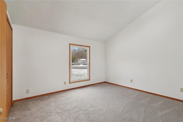 unfurnished room with carpet flooring, baseboards, visible vents, and vaulted ceiling