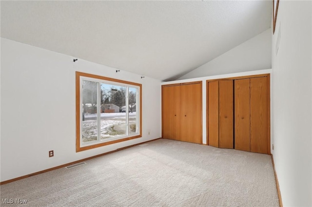 unfurnished bedroom featuring baseboards, visible vents, lofted ceiling, light carpet, and two closets