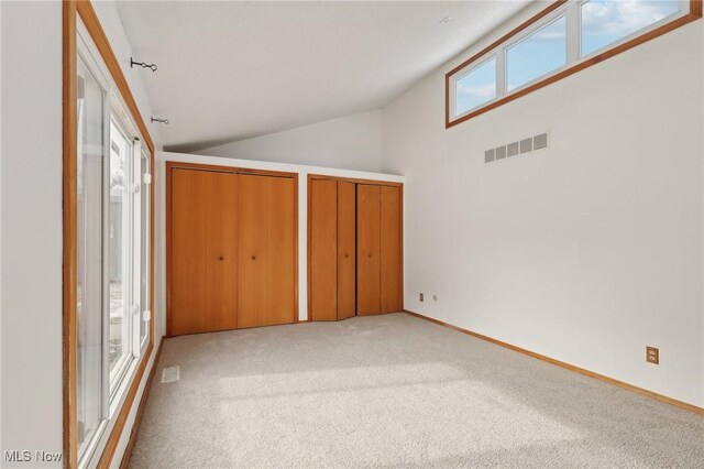 unfurnished bedroom with visible vents, multiple closets, baseboards, light colored carpet, and vaulted ceiling