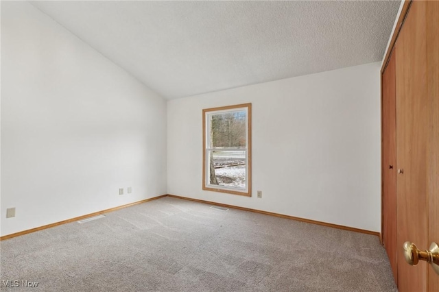 spare room featuring vaulted ceiling, baseboards, carpet floors, and a textured ceiling