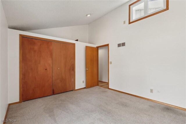 unfurnished bedroom featuring baseboards, visible vents, carpet floors, vaulted ceiling, and a closet