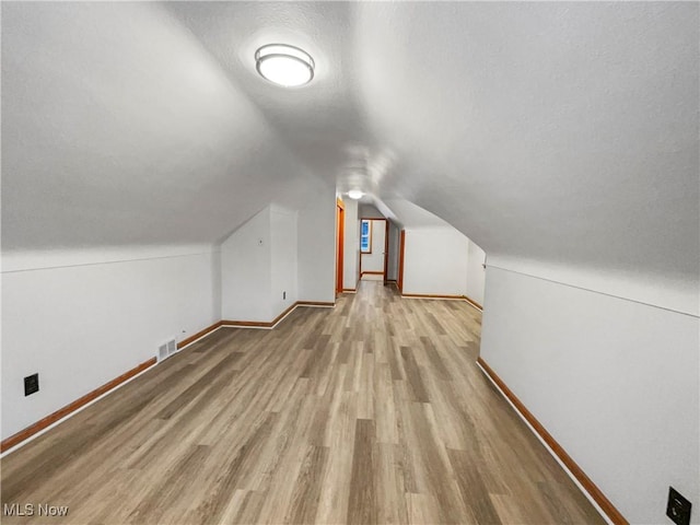 additional living space with baseboards, lofted ceiling, a textured ceiling, and wood finished floors