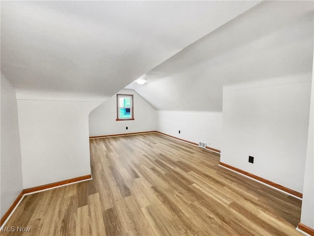 additional living space featuring lofted ceiling, wood finished floors, baseboards, and visible vents