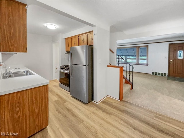 kitchen featuring visible vents, a sink, freestanding refrigerator, light wood finished floors, and gas range