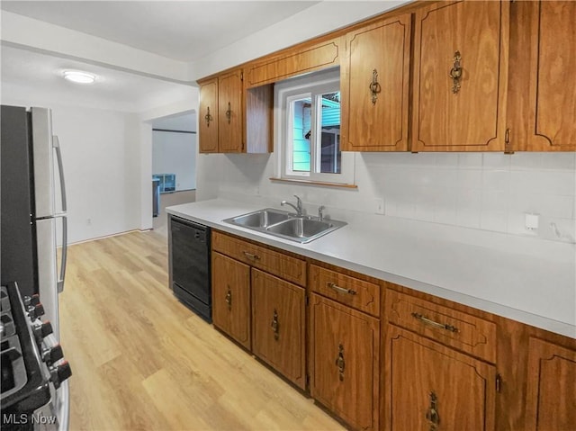 kitchen featuring brown cabinets, freestanding refrigerator, a sink, black dishwasher, and light wood-type flooring