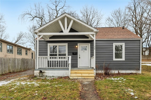 bungalow with covered porch, a shingled roof, and fence