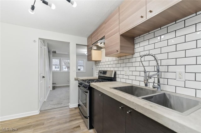 kitchen with under cabinet range hood, gas range, light countertops, decorative backsplash, and a sink