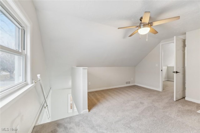 additional living space with visible vents, light carpet, a ceiling fan, baseboards, and vaulted ceiling