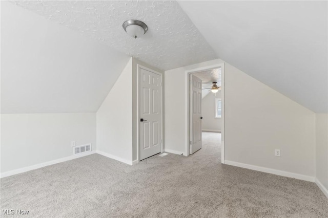 additional living space featuring visible vents, lofted ceiling, a textured ceiling, carpet floors, and baseboards