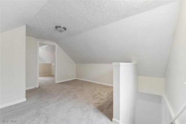 additional living space featuring vaulted ceiling, baseboards, carpet floors, and a textured ceiling