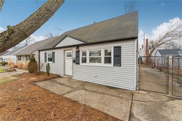 back of house with fence, a shingled roof, and a gate