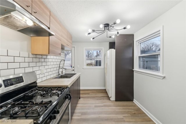 kitchen featuring light brown cabinets, stainless steel range with gas stovetop, freestanding refrigerator, a sink, and under cabinet range hood