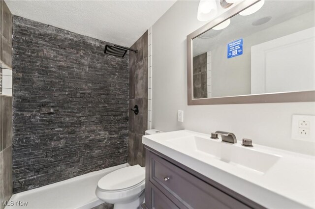 full bath featuring toilet, a textured ceiling, tiled shower, and vanity