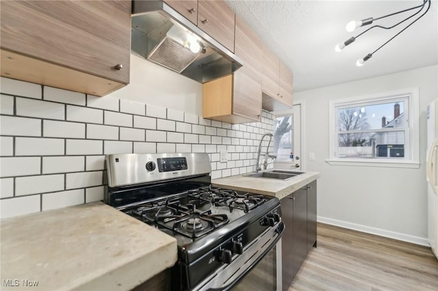 kitchen featuring stainless steel range with gas stovetop, a sink, light countertops, under cabinet range hood, and tasteful backsplash