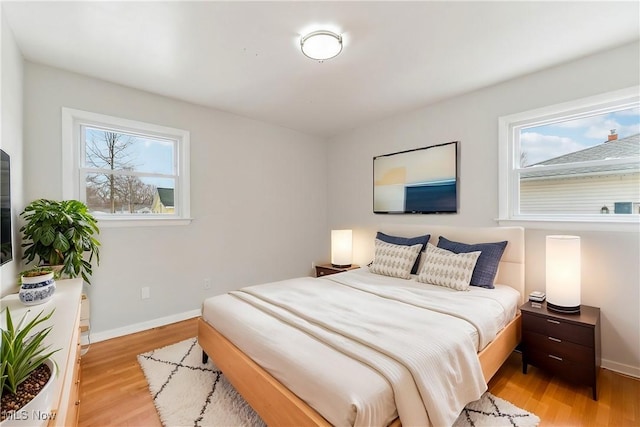 bedroom featuring multiple windows, light wood-type flooring, and baseboards