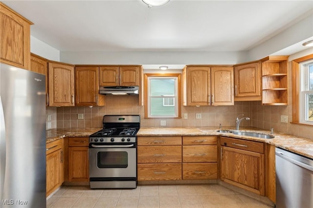 kitchen featuring under cabinet range hood, light stone countertops, appliances with stainless steel finishes, and a sink