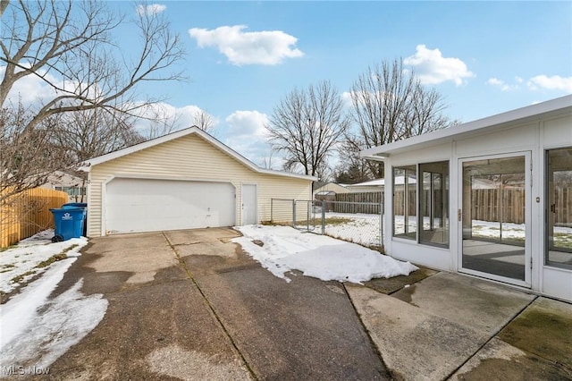 snow covered property featuring a sunroom, a detached garage, an outdoor structure, and fence