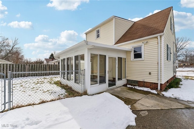 snow covered rear of property with fence and a sunroom