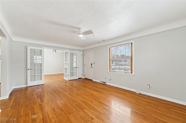 empty room with light wood-type flooring, visible vents, a ceiling fan, french doors, and baseboards