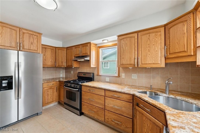 kitchen featuring light stone countertops, under cabinet range hood, decorative backsplash, appliances with stainless steel finishes, and a sink